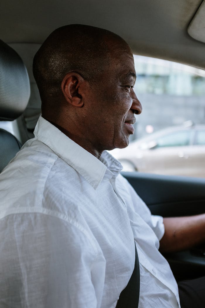 African American man driving a vehicle wearing a white shirt. Urban transportation scene.